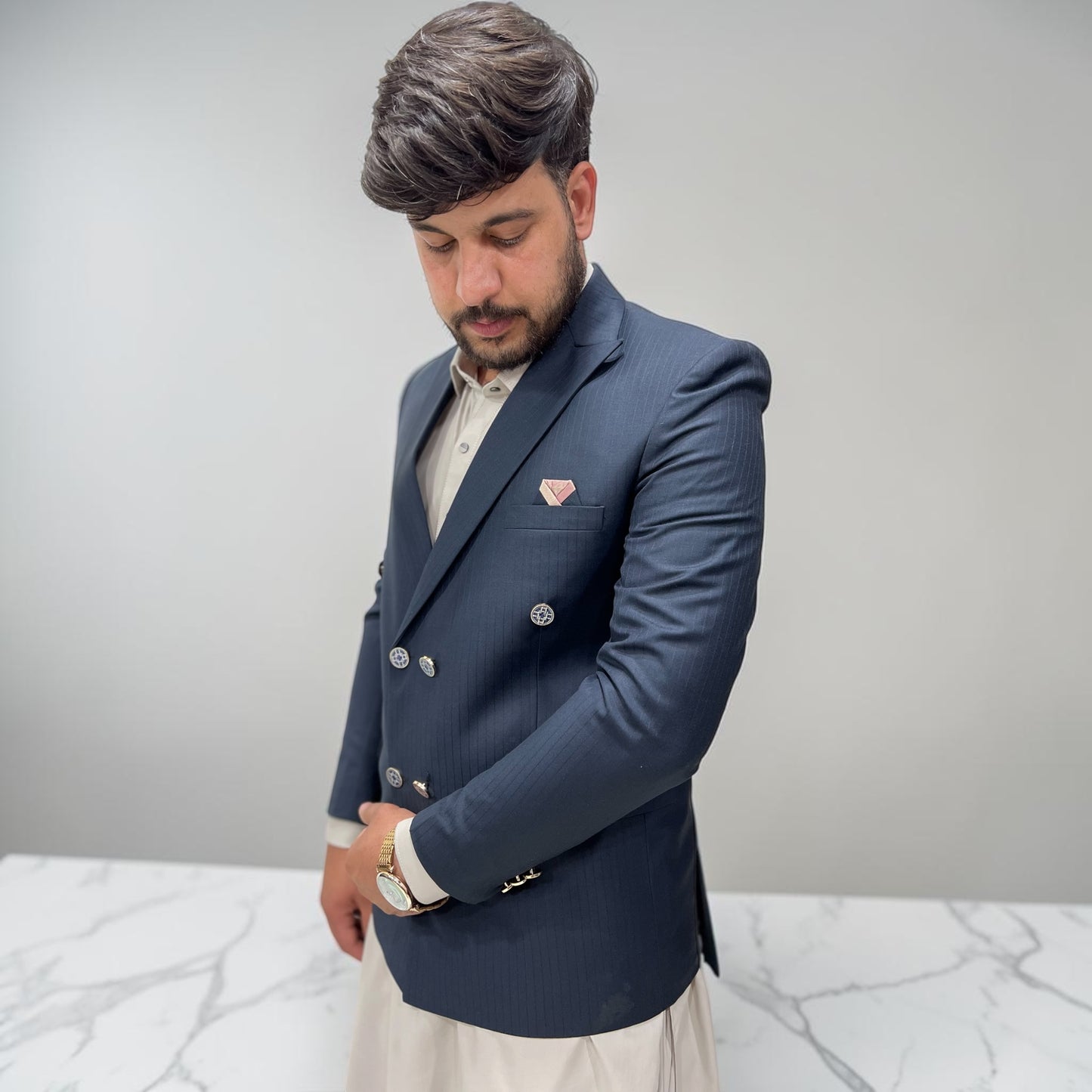 Man wearing a blue blazer with a pink heart pin on a light gray background
