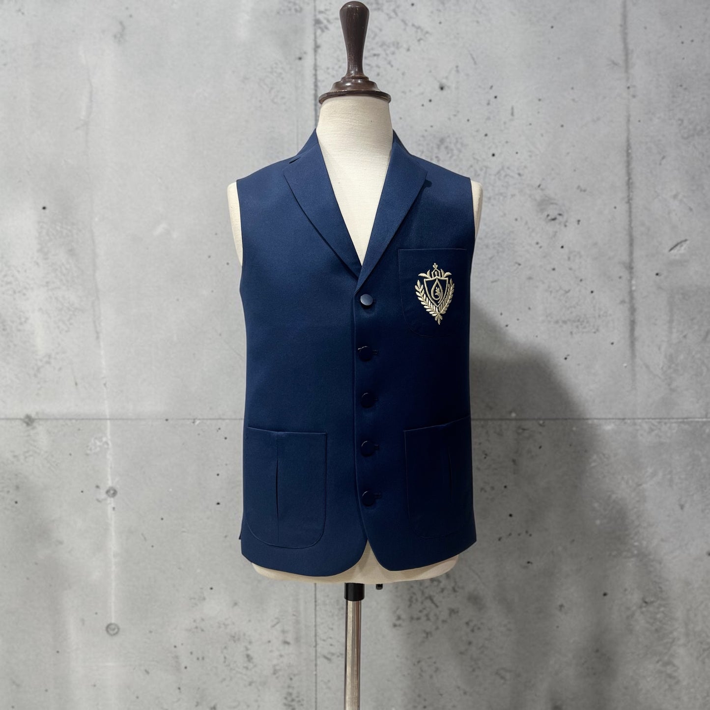 Navy blue vest with a emblem on a mannequin against a concrete wall.