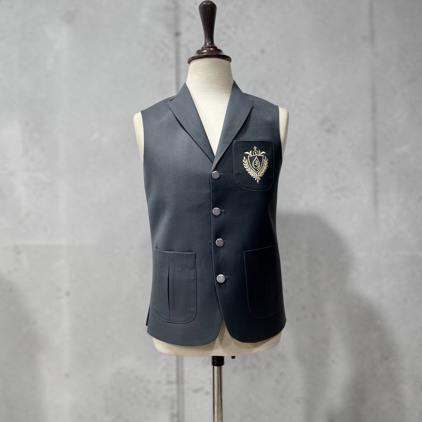 Dark gray vest with a crest on a mannequin against a gray background